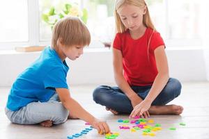 Playing and studying. Two cute little children playing with plastic colorful letters while sitting on the hardwood floor photo