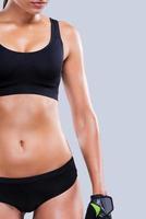 Keeping her body in shape. Close-up of young sporty woman with perfect body standing against grey background photo