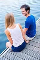 Spending good time together. Top view of beautiful young loving couple sitting at the quayside together and looking at each other with smile photo