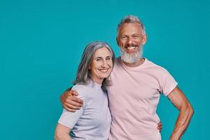 Happy senior couple looking at camera and smiling while standing together against blue background photo