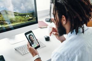 Rear top view of young African man talking with smiling woman using smart phone while sitting indoors photo