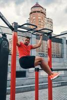 Full length of athletic young man in sports clothing doing pull ups while exercising outdoors on the city street photo