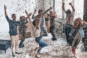 ya es hora de festejar vista superior completa de jóvenes felices gesticulando y sonriendo mientras bailan con confeti volando por todas partes foto