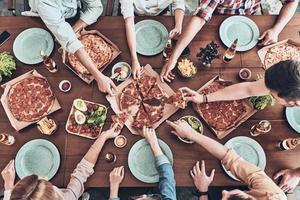 Everybody loves pizza. Close up top view of young people picking pizza slices while having a dinner party in indoors