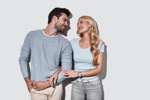 She means everything to him. Beautiful young couple embracing and smiling while standing against grey background photo