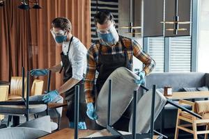 Three male waiters in protective workwear arranging furniture in restaurant photo