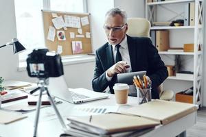 Senior man in elegant business suit using digital tablet while making social media video photo