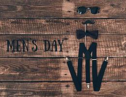 Men's day. High angle shot of suspenders, prop, bow tie and eyewear lying on wooden desk photo