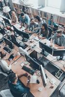 Successful team. Top view of group of young business people in smart casual wear working together while sitting at the large office desk photo