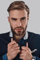 Real macho. Handsome young man looking at camera and adjusting his jacket while standing against grey background photo