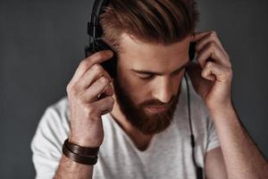 Appreciating his favorite music.  Top view of good looking young man listening music while standing against grey background photo