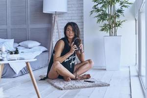 tiempo de buena música. atractiva mujer joven sosteniendo auriculares y mirando hacia otro lado mientras se sienta en el suelo en casa foto