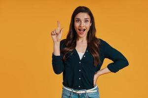 Attractive young woman in casual clothing gesturing and smiling while standing against yellow background photo