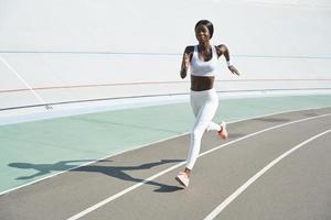 Beautiful young African woman in sports clothing running on track outdoors photo