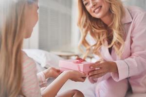 Everything for her princes. Young attractive mother giving a present to her cute little daughter while sitting on the bed at home photo