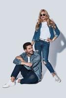 In love with jeans wear. Full length of beautiful young couple bonding while standing against grey background photo