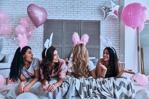 más lindo que cualquier conejito. cuatro hermosas mujeres jóvenes con orejas de conejo pasándoselo muy bien mientras están acostadas en la cama foto