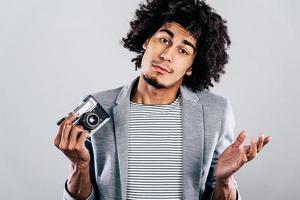 Out of camera film. Handsome young African man holding retro styled camera and looking confused while standing against grey background photo