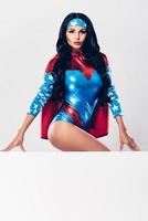 Powerful and seductive. Beautiful young woman in superhero costume looking at camera and leaning over copy space while standing against white background photo