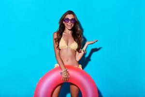 Look over there Attractive young woman in bikini pointing copy space and smiling while standing against blue background photo