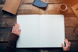 Start planning today. Close-up top view image of woman holding hands over notebook with copy space while sitting at the rough wooden table photo