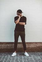 Lost in thoughts. Full length of young mixed race man in casual clothes standing in front of the brick wall and covering face with hand photo