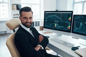 Handsome young man in shirt and tie looking at camera and smiling while working in the office photo