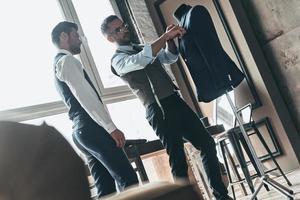 trabajando en diseños de tendencia. dos jóvenes hombres de moda mirando la chaqueta mientras están de pie en el taller