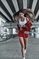 Challenging herself. Full length of attractive young woman in sport clothing keeping eyes closed while running under the bridge outdoors photo