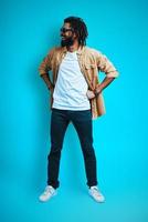 Full length of handsome young African man in casual wear looking away while standing against blue background photo