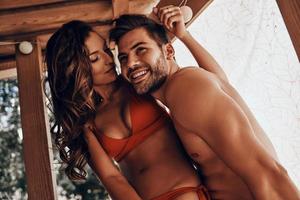 hermosa joven pareja abrazándose y sonriendo mientras descansa en la cabaña de la playa foto