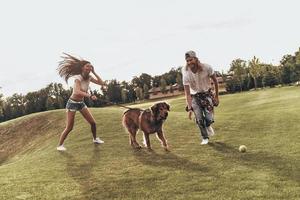 Carefree Sunday. Full length of young modern couple playing with their dog while spending carefree time in the park photo