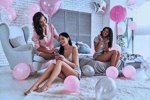 Ladies time. Three attractive young women in pajamas smiling while sitting in the bedroom with balloons all over the place photo