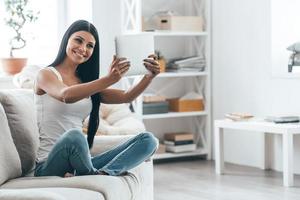 belleza en casa. atractiva mujer joven sosteniendo una tableta digital y sonriendo mientras se sienta en el sofá en casa foto