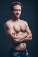 Handsome man. Young shirtless man with serious face keeping arms crossed and looking at camera while standing against black background photo