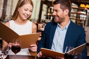 Choosing what to get. Beautiful young loving couple examining menu and smiling while sitting at the restaurant together photo