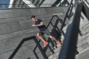 empujando duro para ganar. toda la longitud de un joven con ropa deportiva corriendo por las escaleras mientras hace ejercicio afuera foto