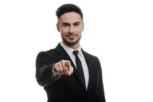 I choose you  Handsome young man in full suit looking at camera and pointing you while standing against white background photo