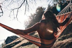 Feeling great.  Rear view of young woman keeping arms outstretched while relaxing in hammock outdoors photo