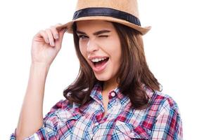 belleza parpadeante. hermosa mujer joven con ropa funky ajustando el sombrero y guiñando un ojo a la cámara mientras está de pie contra el fondo blanco foto