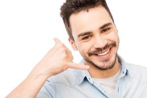 Waiting for your call. Confident young man in shirt gesturing mobile phone near his face and smiling while standing against white background photo