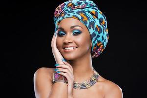 In love with her style. Beautiful African woman wearing a headscarf and jewelry and smiling while standing against black background