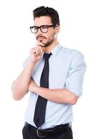 Waiting for inspiration. Thoughtful young man in shirt and tie looking away and touching his chin while standing against white background photo