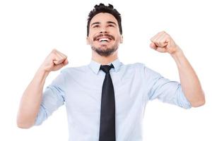 joven y exitoso. joven feliz con camisa y corbata manteniendo los brazos levantados y sonriendo mientras está de pie contra el fondo blanco foto