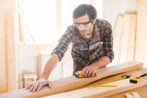 Everything should be perfect. Concentrated young male carpenter in protective eyewear working in his workshop photo