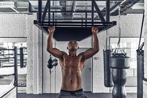 entrenamiento de la mañana. apuesto joven africano haciendo pull-ups mientras hace ejercicio en el gimnasio foto