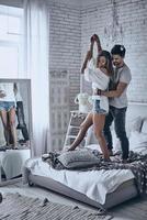 él nunca la dejará ir. toda la longitud de una pareja joven y juguetona tomándose de la mano y uniéndose mientras bailan en la cama en casa foto