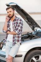 I have some road troubles. Serious young man talking on the mobile phone while leaning a vehicle hood photo