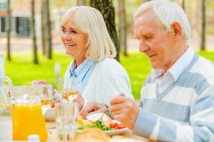 Enjoying dinner outdoors. Senior couple enjoying meal together while sitting at the dining table outdoors photo