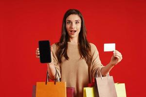 Surprised young woman in casual clothing carrying shopping bags and making a face photo